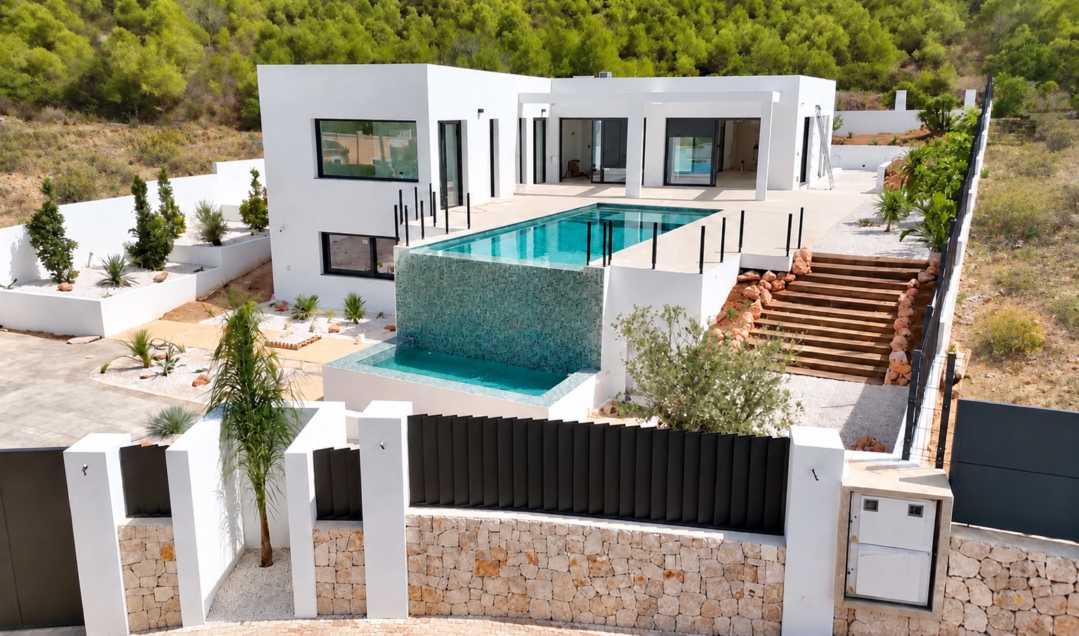 Casa Valsol — a completed contemporary white villa with a turquoise infinity-edge pool and waterfall, terraced patio and landscaped garden, set against protected green hillside